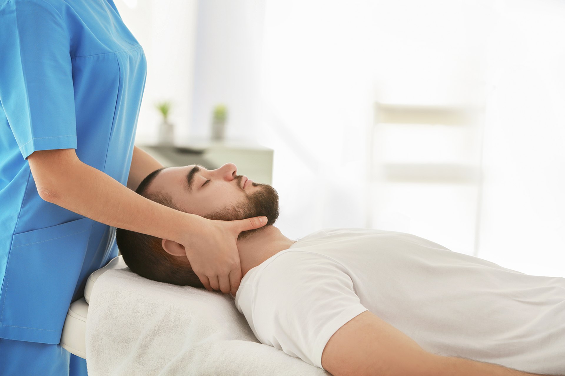 A chiropractor adjusts a mans neck while he lies on an examination table.